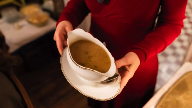 Mujer llevando una salsera a la mesa de Navidad / Canva