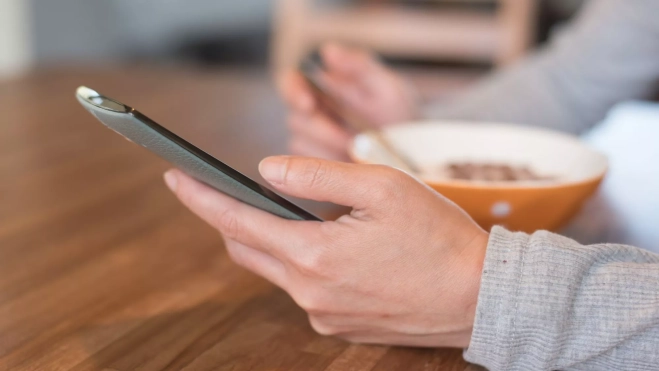 Persona comiendo con el teléfono móvil en la mano / Canva