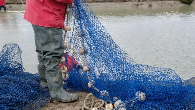 Pescador preparando las redes de pesca en el puerto / Canva